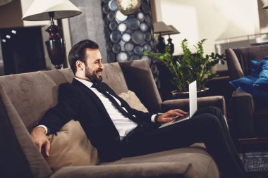 Yakışıklı adam salonda dizüstü bilgisayarını kullanarak ve memnun arıyorum