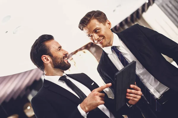 Улыбающийся человек смотрит на своего делового партнера, стоя с современным устройством — стоковое фото