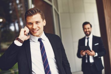 Kendine güvenen genç adam cep telefonu ile ayakta ve gülümseyerek