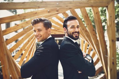Arkalarında ahşap yapı ile arka arkaya duran kendine güvenen arkadaşlar