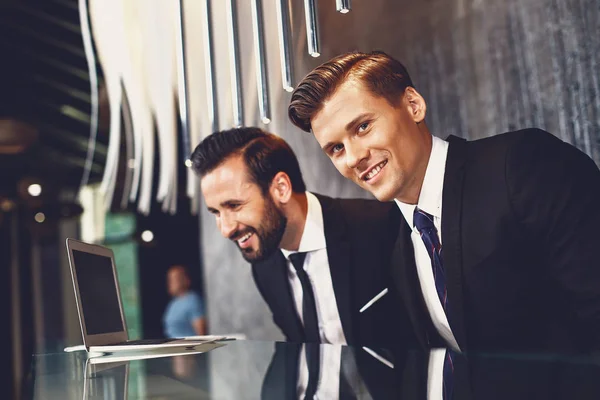 Sonriente hombre mirando el portátil mientras su colega de pie cerca — Foto de Stock