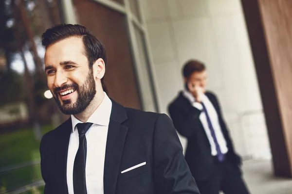 Close up of smiling man with his friend talking on the phone in the background — Stock Photo, Image