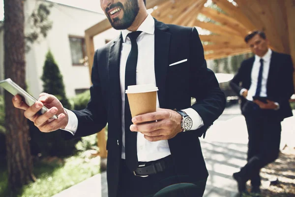 Joven sosteniendo la taza de café mientras está de pie con el teléfono inteligente — Foto de Stock