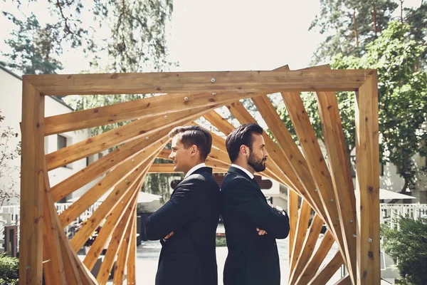 Two men standing with their backs to each other next to the wooden construction