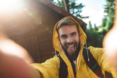 Gezgin adam ahşap evin yakınında komik bir selfie çekiyor.