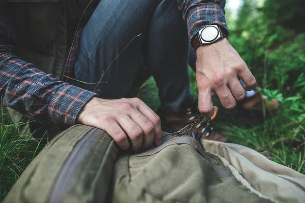 Traveler man zipping his backpack on green grass