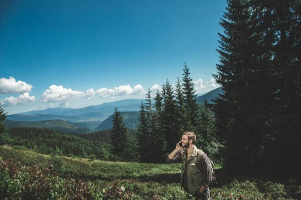 Traveler man talking by phone on green hill