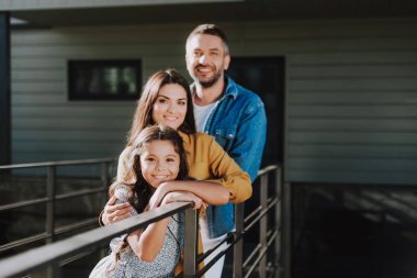 Kızıyla birlikte gülümseyen çift dışarıda bekliyor.