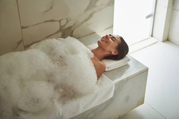 Pozytywna kobieta leżąca w piance mydlanej i uśmiechnięta szczęśliwie podczas przyjemnego zabiegu — Zdjęcie stockowe