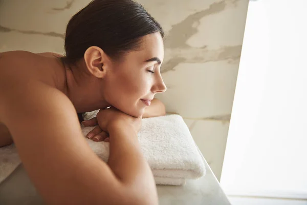 Bonita jovencita sonriendo alegremente y mirándote tumbada sobre la toalla en el baño turco — Foto de Stock