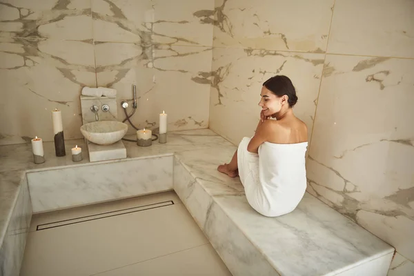 Senhora de cabelos escuros sorrindo enquanto vestindo toalha branca em hammam — Fotografia de Stock