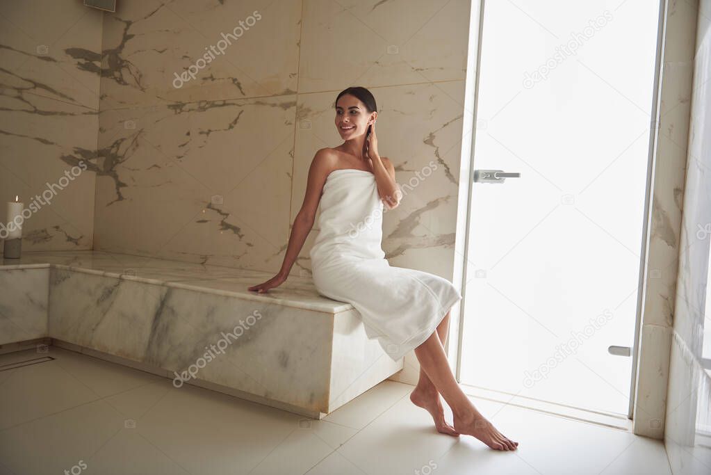 Cute lady touching her neck while sitting on marble surface