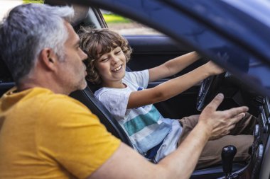 Beyaz, yetişkin bir adam arabada el kol hareketi yapıyor.