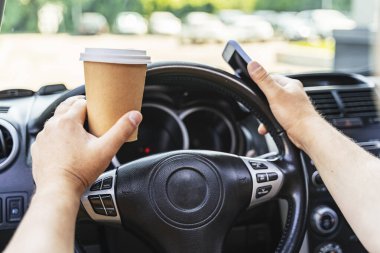 Kafkasyalı bir adam arabasını sürüyor ve kahve içiyor.