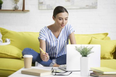 Kanepede dizüstü bilgisayarda gülümseyen kadın.