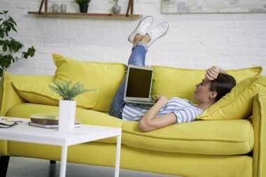 Kanepede dizüstü bilgisayarda çalışan yorgun kadın.