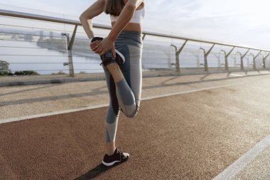 Genç atletik bayan dışarıda bacaklarını esnetiyor.