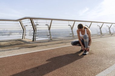 Atletik kadın ayakkabılarına bağcık bağlamak için çömeliyor