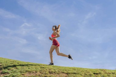 Yeşil tepede spor yapan atletik kadınlar var.