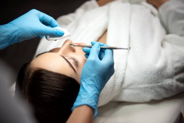 Steril eldivenli bir güzellik uzmanı, temizlikçi kadın yüzü için siyah başlık çıkarıcı kullanıyor.