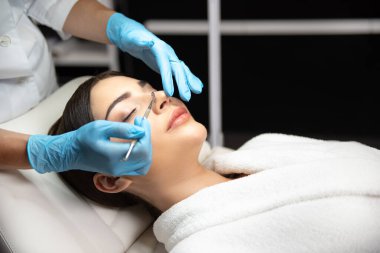 Kozmetikçi, siyah başlık çıkarıcıyla kadın yüzündeki kirliliği temizliyor.