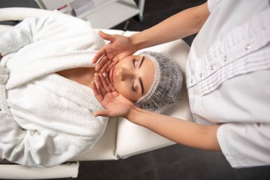 Güzeller güzeli genç bir kadın güzellik salonunda yüz masajı yaptırıyor.