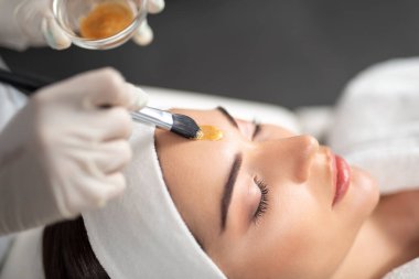 Kadın yüzüne kozmetik maske takan steril eldivenli bir güzellik uzmanı.