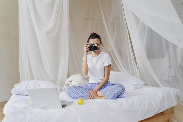 Mujer joven está sentada en el dormitorio con la cámara —  Fotos de Stock