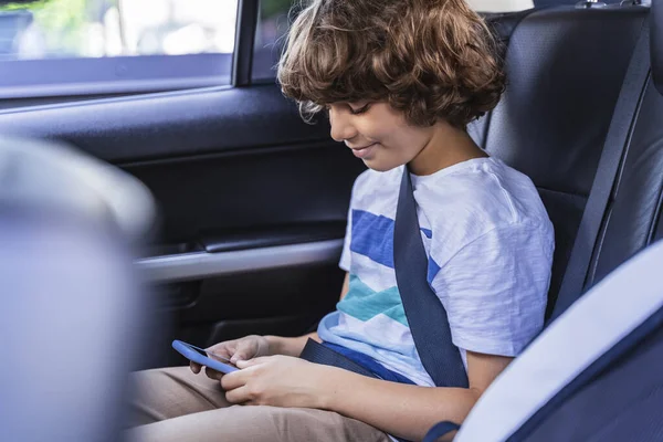 Garotinho sorridente está jogando no smartphone no carro — Fotografia de Stock