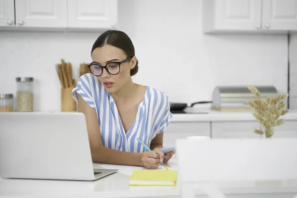 Arbetskvinna gör anteckningar och tittar på laptop lager foto — Stockfoto