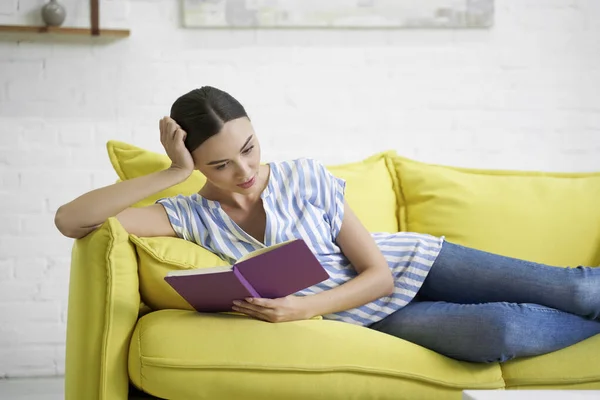 Спокійна жінка читає свій щоденник на дивані фото — стокове фото