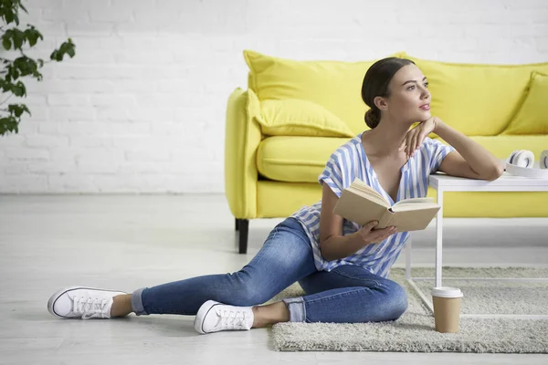 Verträumte Dame mit einem Buch am Couchtisch Archivfoto — Stockfoto