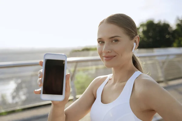 Jeune femme athlétique heureuse montrant téléphone mobile — Photo