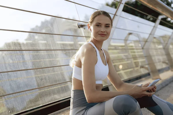 Deportiva dama sentada con teléfono móvil al aire libre —  Fotos de Stock