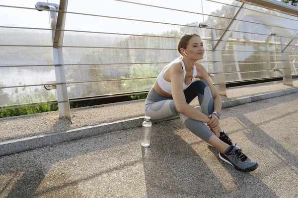 Señora feliz en ropa deportiva sentado en el camino del puente — Foto de Stock