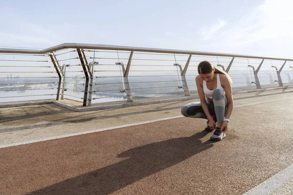 Atletik kadın ayakkabılarına bağcık bağlamak için çömeliyor
