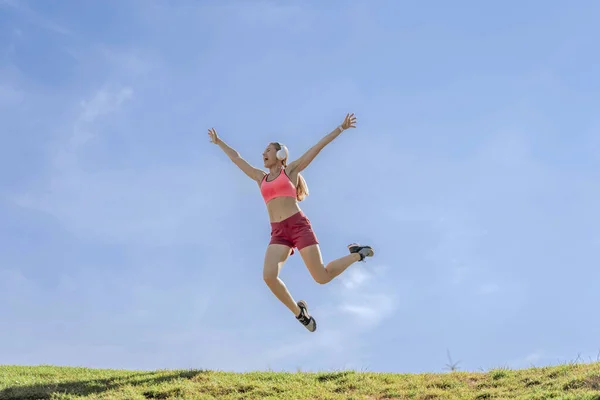Radosna sportowa pani skacząca na zielone wzgórze — Zdjęcie stockowe