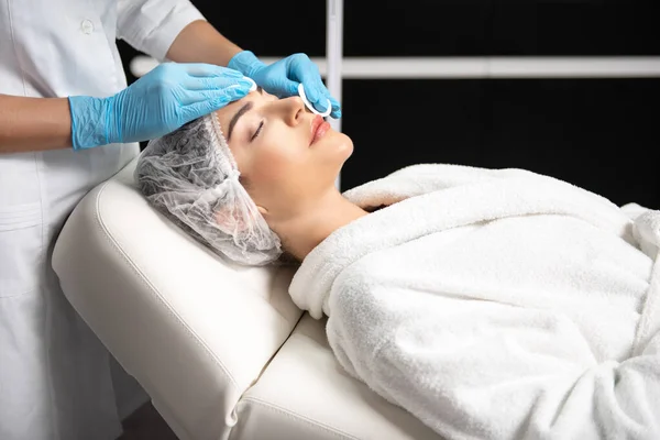 Kobieta kosmetyczka w sterylnych rękawiczkach oczyszczająca twarz pani z podkładkami bawełnianymi — Zdjęcie stockowe