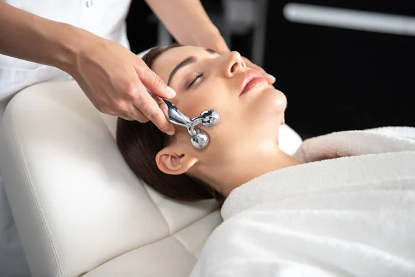 Mujer joven y serena recibiendo masaje facial en el salón de belleza — Foto de Stock