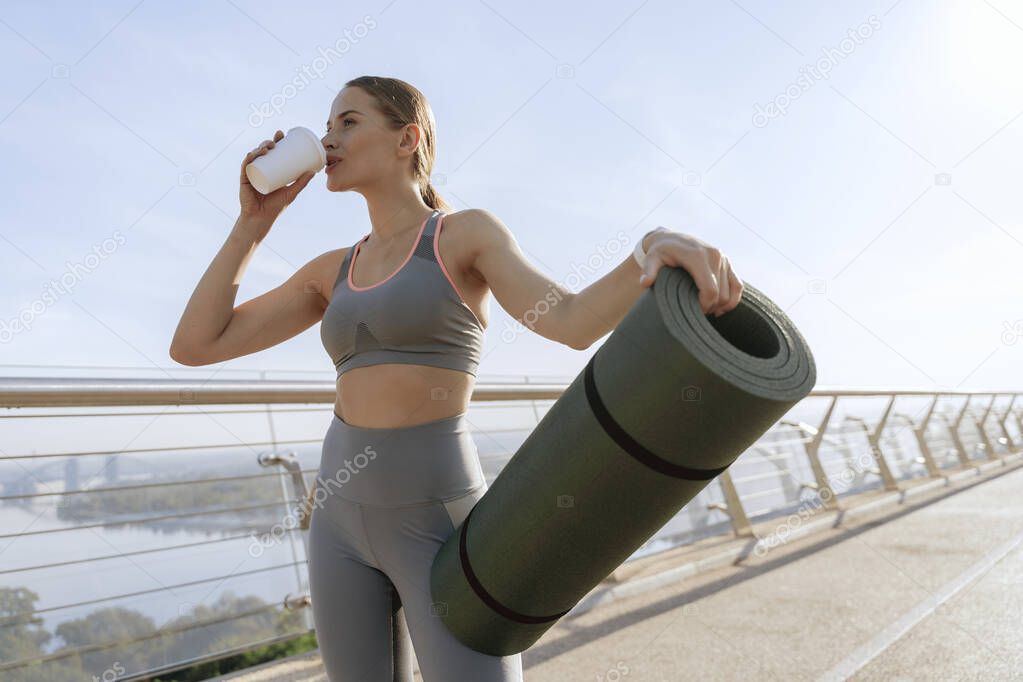 Young lady with roll mat drinking coffee