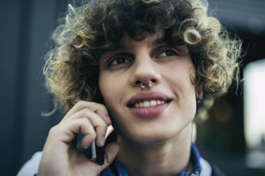 Neşeli kıvırcık adam dışarıda akıllı telefondan konuşuyor.