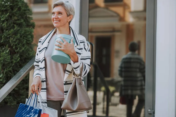 Uśmiechnięta starsza pani stojąca w pobliżu butiku — Zdjęcie stockowe