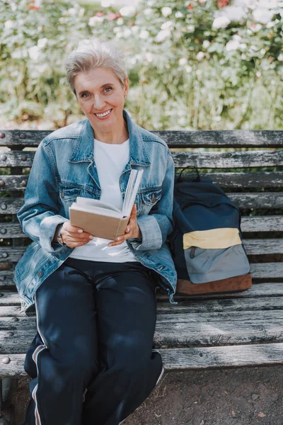 Señora alegre sentada con un libro al aire libre — Foto de Stock