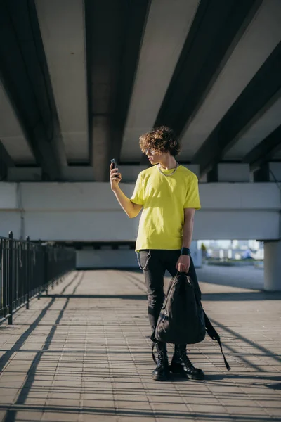 Chico rizado con mochila y teléfono inteligente en streen stock foto — Foto de Stock