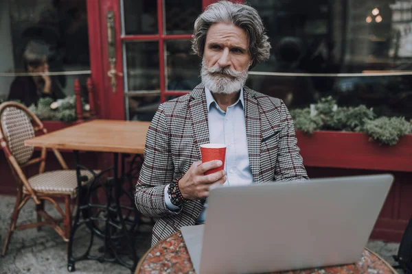 Задумчивый бородатый мужчина с кофе и ноутбуком фото — стоковое фото