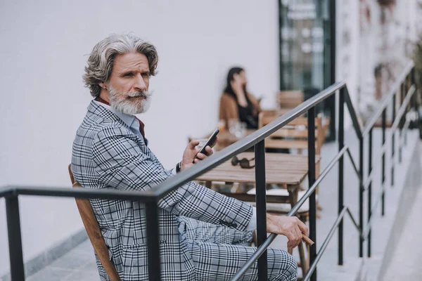 Hombre serio con teléfono inteligente y cigarro sentado solo stock foto — Foto de Stock