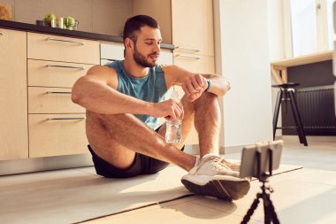 Atletik genç adam kol saatine bakıyor ve gülümsüyor.