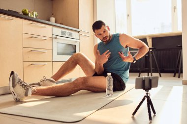 Atletik genç adam evden online antrenman dersi veriyor.