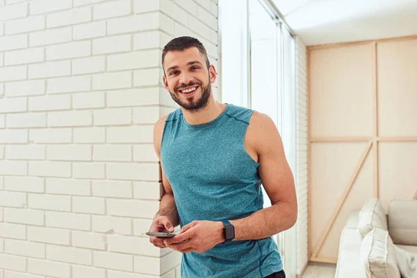 Joven alegre usando un teléfono inteligente moderno en casa — Foto de Stock