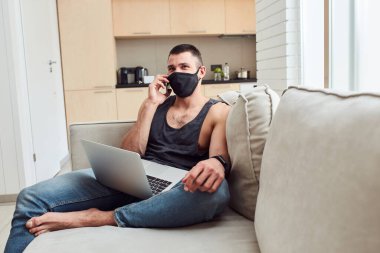 Tıbbi maskeli yakışıklı beyefendi cep telefonuyla konuşuyor.